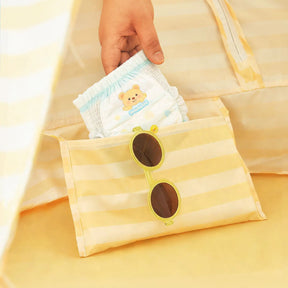 A hand places a bear-design baby diaper and yellow sunglasses into the Tiny Land® One-Stop Beach Toy & Tent Set – Pastel Yellow Stripes, perfect essentials for fun under UV protection in this kids' beach tent.