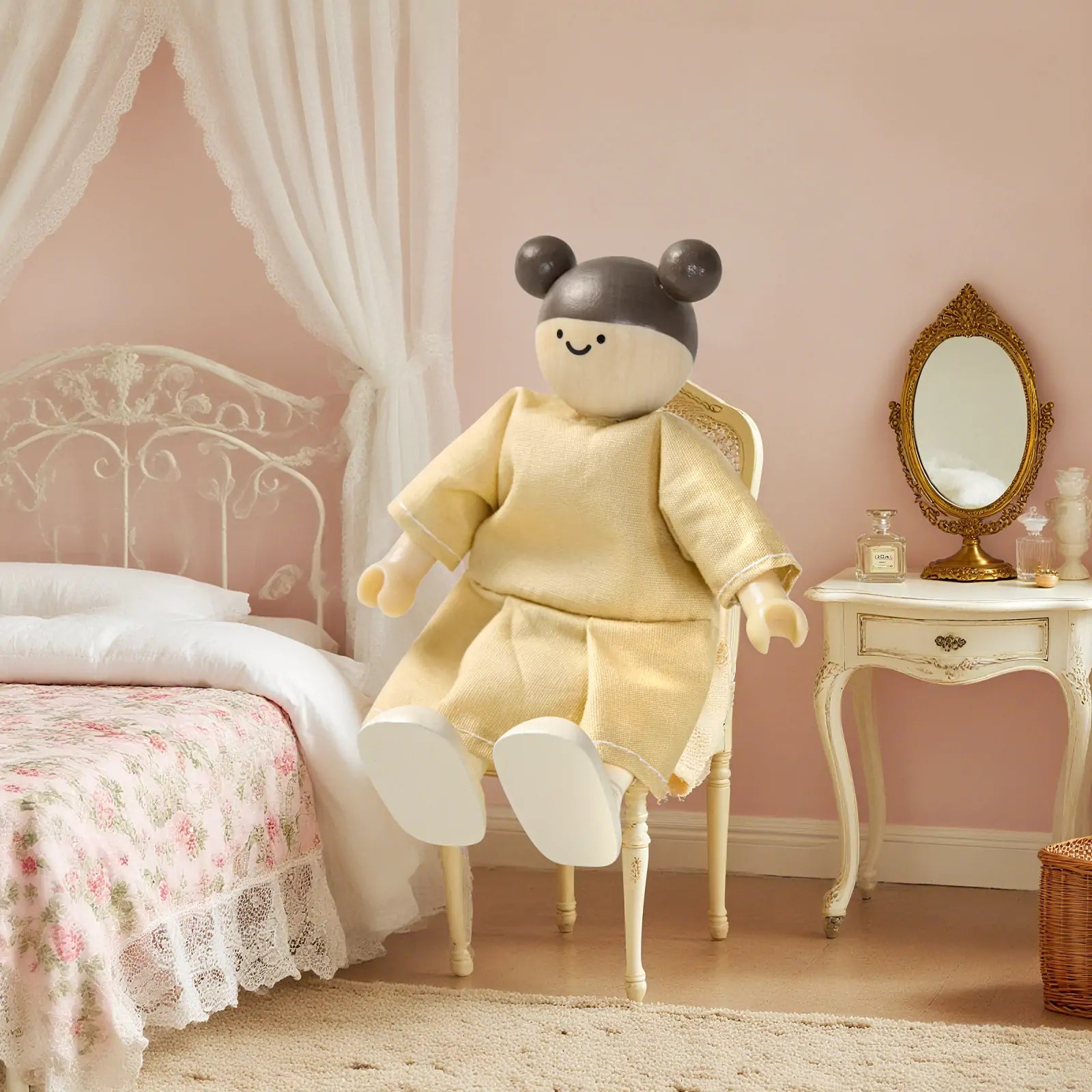 A Tiny Land® Wooden Dollhouse Doll by Tiny Land INC, featuring round black ears and a beige dress, sits on a chair in a pastel pink bedroom with a floral bedspread, white canopy bed, and antique-style vanity with oval mirror.