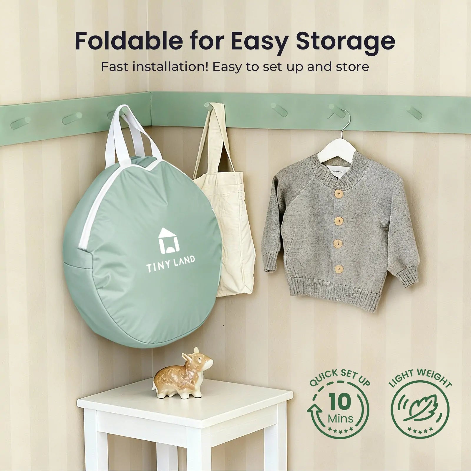 A sage green Tiny Land® Compact Adventure 3-in-1 Play Tunnel (no balls) hangs on a wall hook next to a child’s gray sweater, with a decorative hippo below. Lightweight and easy to set up—perfect for storing your play tunnel.