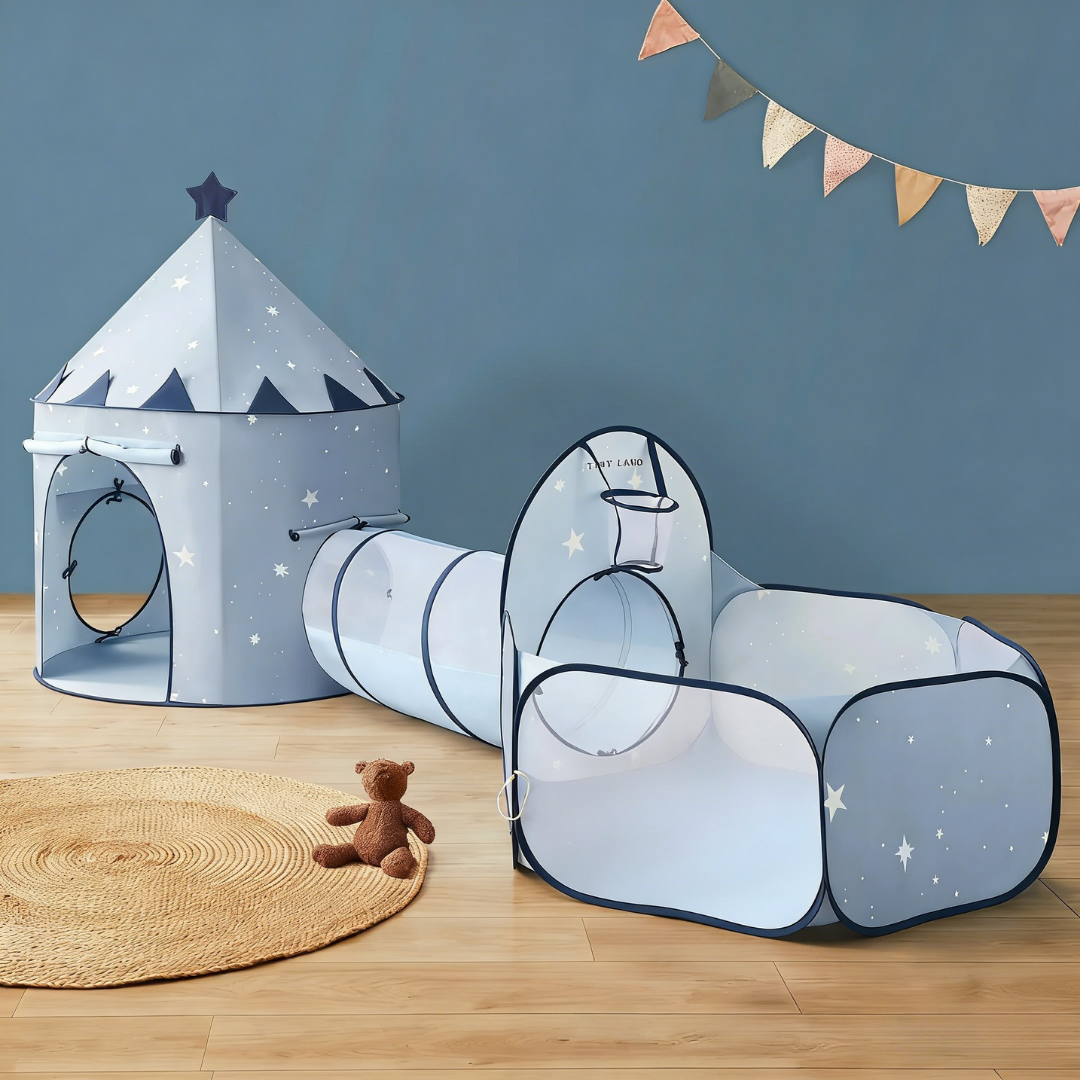 The Tiny Land® Compact Adventure 3-in-1 Play Tunnel With no Balls - Blue, shaped like a starry castle and connected to a tunnel and ball pit, sits on a wooden floor beside a round rug, a brown teddy bear, and colorful pennant banners above.