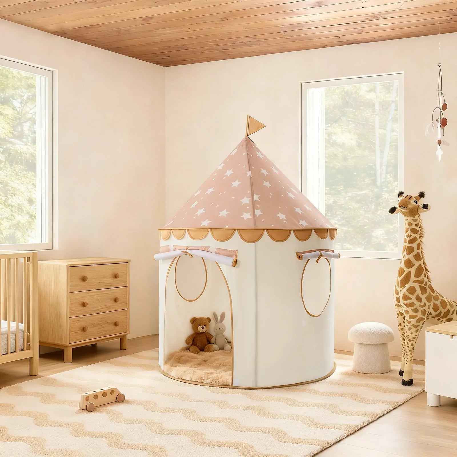 A cozy, light-filled nursery features the Tiny Land® Cheerful Pennant Castle Tent, a crib, dresser, plush giraffe, soft rug, and stuffed toys—all in neutral and pastel tones with wooden accents.