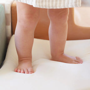 A close-up shows a young child’s bare legs and feet on a soft, white Tiny Land® PlayNest Climbing Block by Tiny Land INC, partially covered by a light garment.