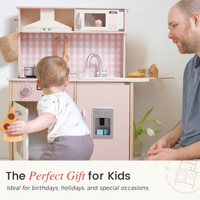 A toddler delights in imaginative play with the Tiny Land® PopJoy Play Kitchen—shown here in a charming pink and white design—while an adult looks on, smiling warmly. The child holds a toy pizza slice, discovering endless possibilities with their Tiny Land mini kitchen. Text below highlights the PopJoy Play Kitchen as a wonderful gift choice for kids.|Pink