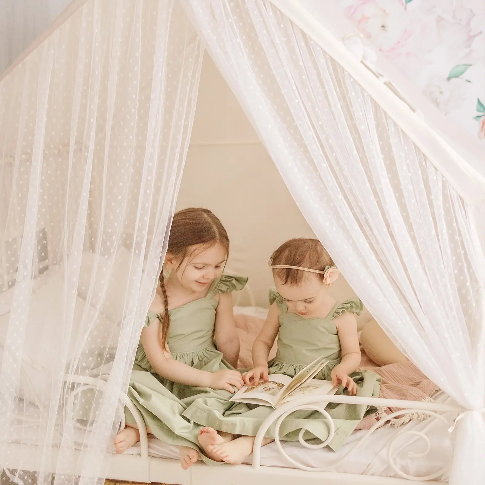 Two young children in matching green dresses read together inside the Tiny Land® Large Space Play House with Star Lights by Tiny Land, enjoying a cozy, gentle atmosphere with soft lighting and floral decor above the bed.
