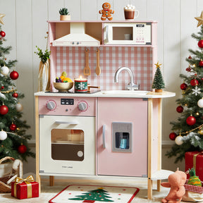A festive Christmas scene features the Tiny Land® PopJoy Play Kitchen in pink and green by Tiny Land, adorned with a gingerbread figure, miniature Christmas tree, and playful utensils. The charming setup is surrounded by flanking Christmas trees, a gift box, and a reindeer rocker atop a cheerful holiday rug.|Pink