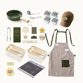 A flat lay featuring the Tiny Land® BistroSwitch Play Kitchen by Tiny Land—complete with green pan, utensils, loaf trays, striped apron, and cooktop—perfect inspiration for kids' pretend play with fun badges, cards, and stickers.|Green
