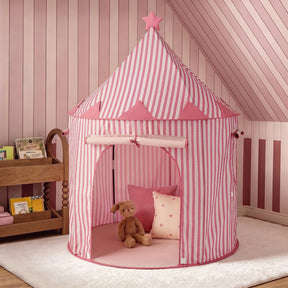 A Tiny Land® Kids Tent – Indoor Tent for Toddlers by Tiny Land, featuring pink and white stripes with a star on top, sits on a white rug. Inside the tent are a brown stuffed bunny and a pink pillow. Nearby, a wooden shelf displays children’s books. The room’s pink striped and paneled walls create the perfect setting for this charming indoor play tent or playhouse for kids.|PInk