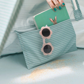 A hand with teal-painted nails holds a notebook near the Tiny Land® One-Stop Beach Toy & Tent Set – Sea Blue, with pink flower-shaped sunglasses and scattered sand adding to the relaxing beach vibe.
