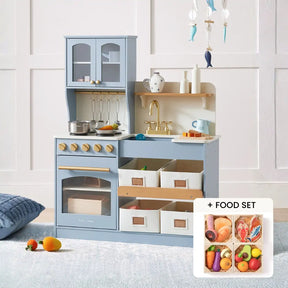 The Tiny Land® Serenity Wooden Kitchen & Wooden Food Set by Tiny Land features a light blue kitchen with shelves, bins, sink, and stove. It comes with utensils, pots, and colorful pretend food. Shown against a white wall with a nearby cushion.