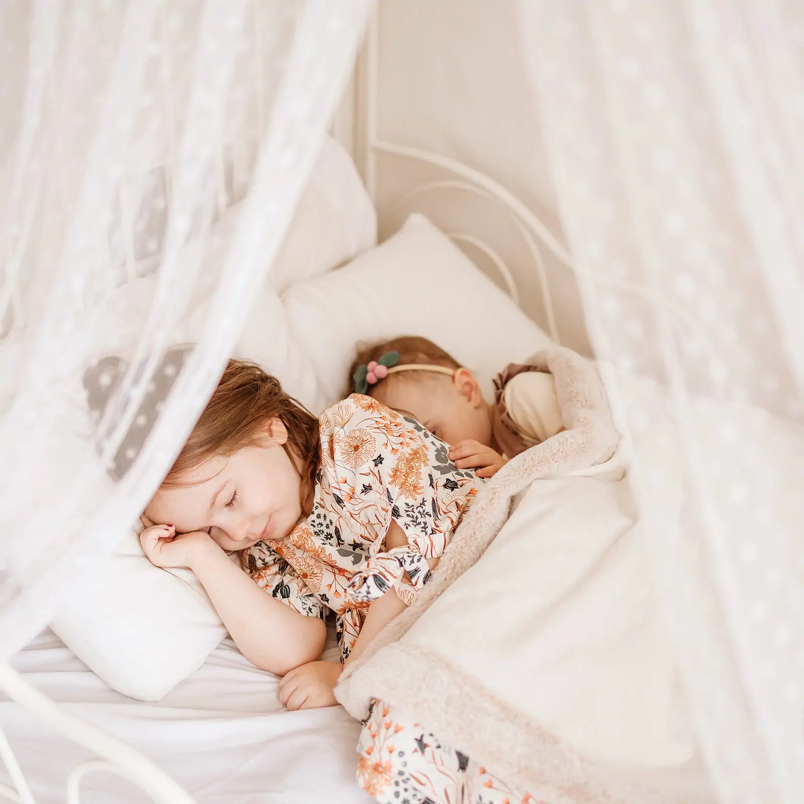 Two young children sleeping peacefully under the sheer white canopy of a Tiny Land Cozy Nook Bundle in a cozy play nook.|Mesh