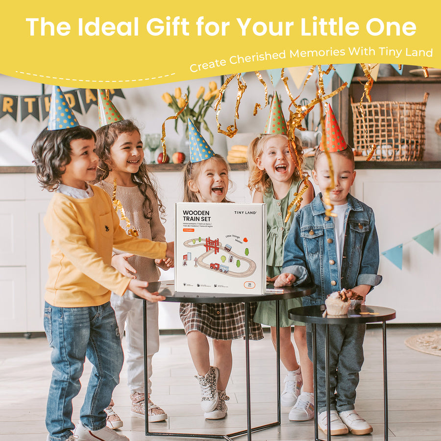 Four children in party hats smile around a gift box labeled "Tiny Land® Wooden Train Set for Children 39 Pcs" by Tiny Land, placed on a table. The festive background features colorful decorations and golden streamers.|39 Pcs