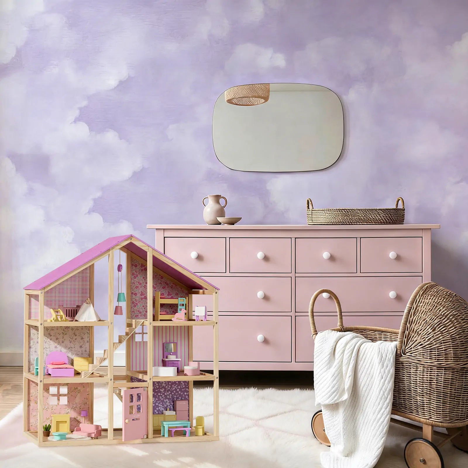 A pastel-themed child’s room featuring a pink dresser, Tiny Land® Sweetwood Unicorn Dollhouse & Wooden Dollhouse Dolls, a wicker bassinet with a white blanket, and a mirror on a cloud-painted purple and white wall.