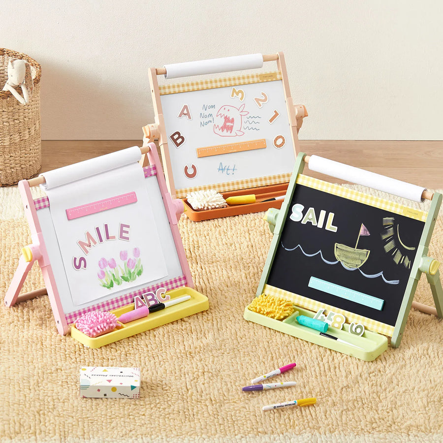 Three Tiny Land® Double-Sided Magnetic Tabletop Easels by Tiny Land, including an adjustable kids’ easel with a magnetic whiteboard, display colorful drawings and words. Each art station features storage trays holding chalk, erasers, and crayons—all set on a beige carpet in a cozy playroom setting.