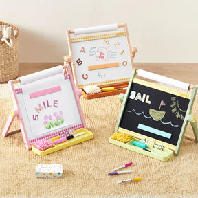 Three Tiny Land® Double-Sided Magnetic Tabletop Easels by Tiny Land, including an adjustable kids’ easel with a magnetic whiteboard, display colorful drawings and words. Each art station features storage trays holding chalk, erasers, and crayons—all set on a beige carpet in a cozy playroom setting.