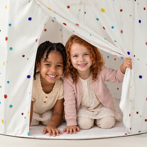 Two young girls smiling while sitting inside a Tiny Land® Compact Adventure 3-in-1 Play Tunnel white play tent with colorful polka dots and a connected play tunnel.|Colorful Dots