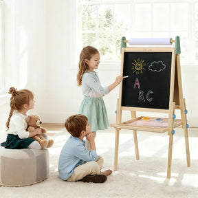 Three young children are in a bright room. One girl uses the Tiny Land® 3-in-1 Art Easel for Kids - Morandi by Tiny Land to draw, while another girl hugs a teddy bear and sits on the floor with a boy watching her.