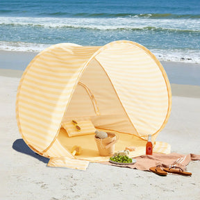 The Tiny Land® One-Stop Beach Toy & Tent Set in pastel yellow stripes keeps your towel, sandals, sunglasses, grapes, drink, woven bag, and sand play set cool and safe with UV protection by the ocean.