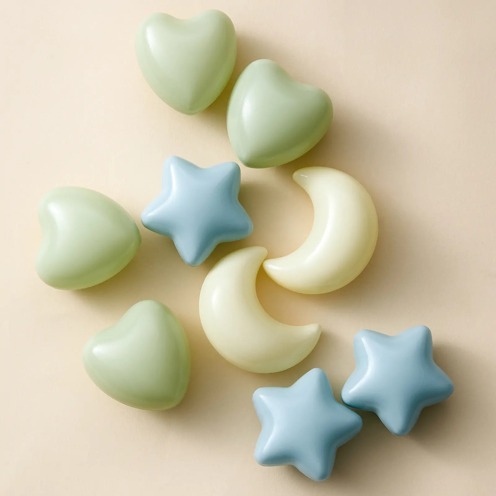 Pastel heart, star, and moon shapes from the Tiny Land® Green Adventure 3-in-1 Play Tunnel & Fun-Shapes Ocean Ball Set are arranged on a light beige surface, creating a soft, playful pattern reminiscent of sensory play.