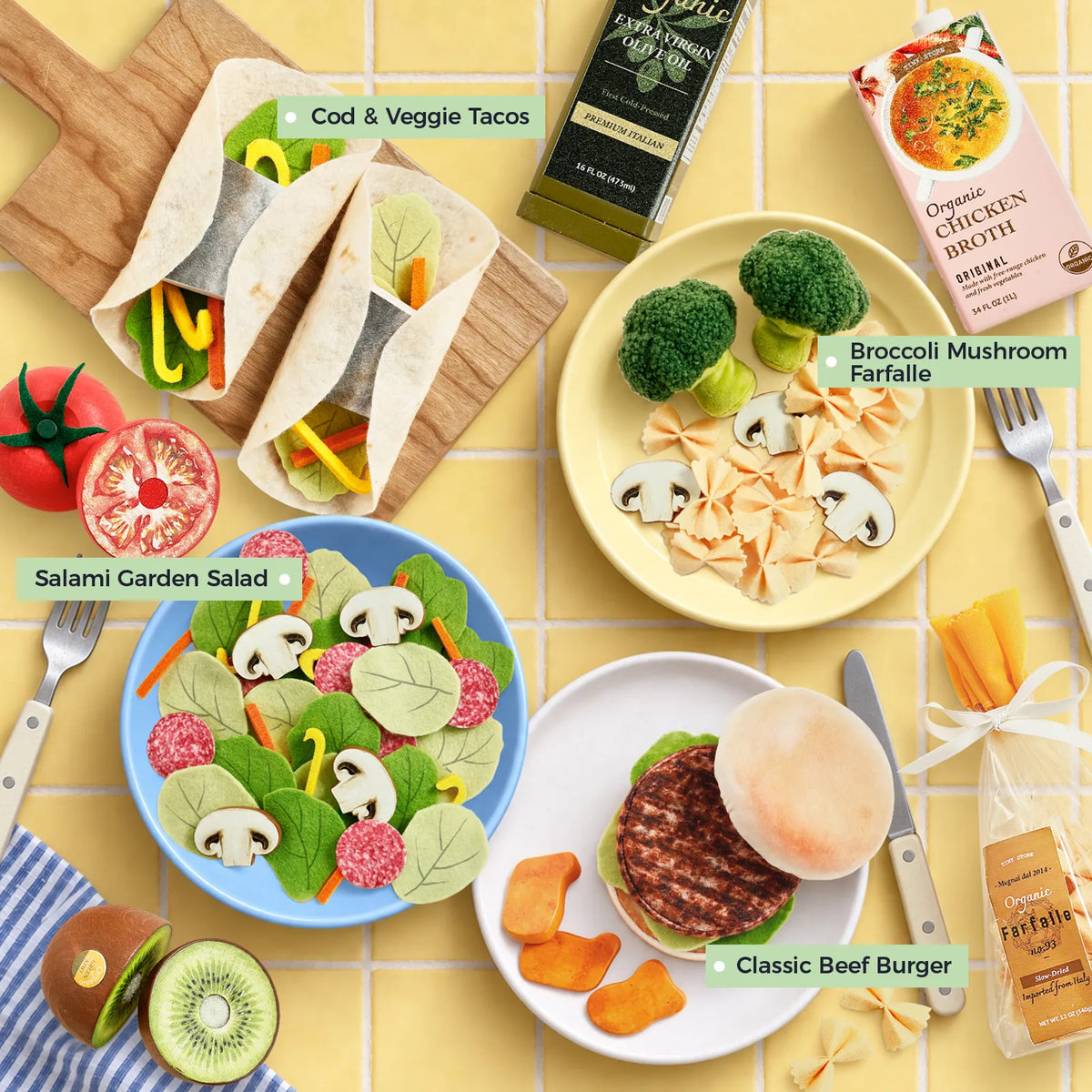 Four plates of food arranged on a yellow tiled surface, each labeled Cod & Veggie Tacos, Broccoli Mushroom Farfalle, Salami Garden Salad, and Classic Beef Burger, with fresh ingredients scattered nearby—perfect for inspiring imaginative pretend play food adventures or adding to a kitchen play set as part of the Tiny Land® Complete Cooking Play Food Set by Tiny Land.