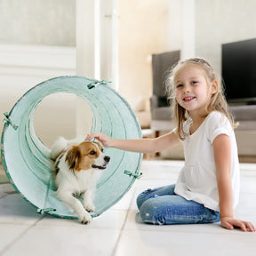 A young girl smiles as she pets a small dog peeking out from the Tiny Land® Adventure Play Tunnel - Green by Tiny Land in a bright, modern living room.|green