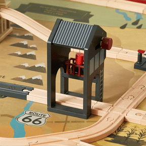 The Tiny Land® 1920 Railway Adventure Train Table by Tiny Land INC features a wooden train set, black and gray drawbridge over tracks, and a Route 66 sign on the playmat for interactive city railway fun.