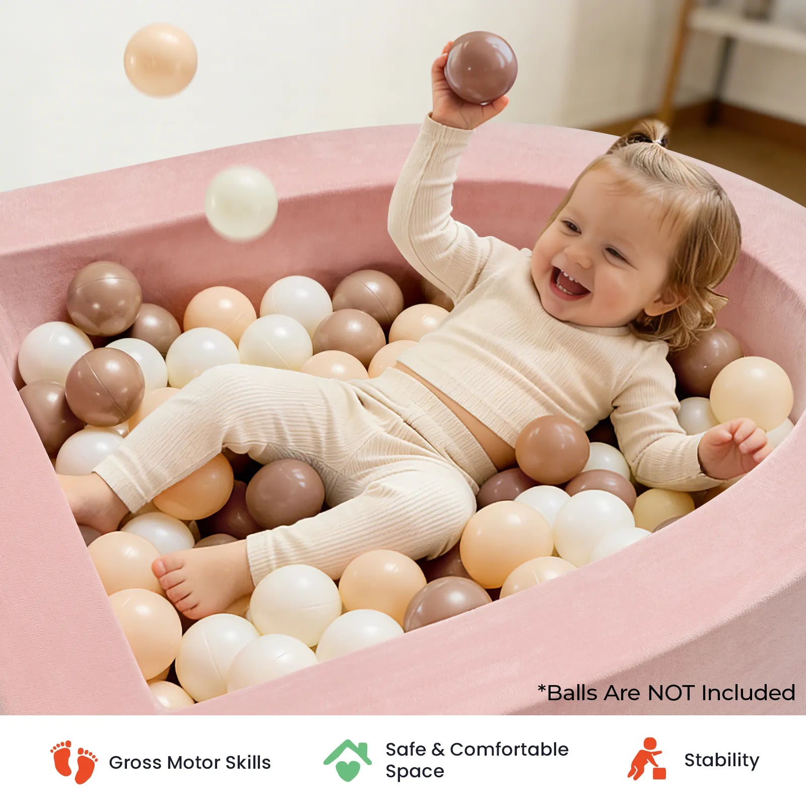 A smiling toddler in beige clothes sits in the pink Tiny Land® PlayNest Soft Foam Ball Pit by Tiny Land, surrounded by white, beige, and brown balls (balls not included), holding one up. Perfect for sensory play in any toddler playroom, this setup encourages motor skill development, safety, and stability—highlighted by icons below.|Pink