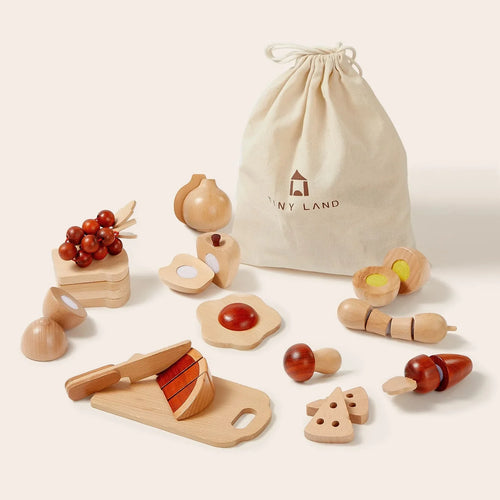 Tiny Land Play Food’s Wooden Cut and Play Food Toy Set features play kitchen accessories—fruits, veggies, cheese, eggs, a knife, and cutting board—displayed before a beige “Tiny Land” drawstring bag.