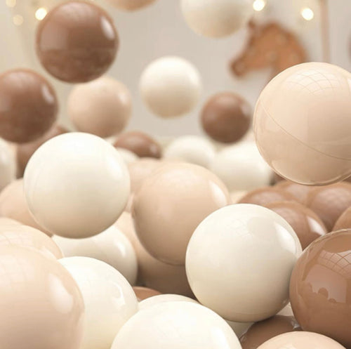 A set of 200 non-toxic Tiny Land® Ocean Balls in white, beige, and brown float and pile in a soft play area. Behind them, a wall with horse decor and string lights adds charm to the scene.