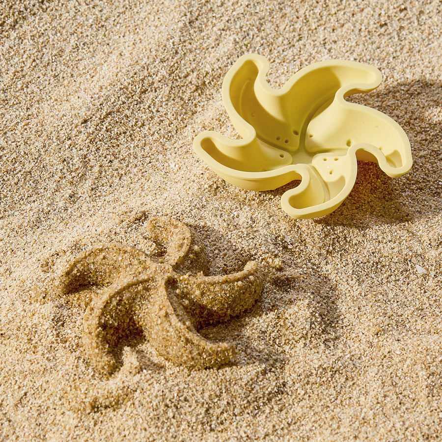 A yellow star-shaped mold from the Tiny Land® Sand-Buddies Sand Toy Set by Tiny Land sits on the sandy beach beside its matching impression.