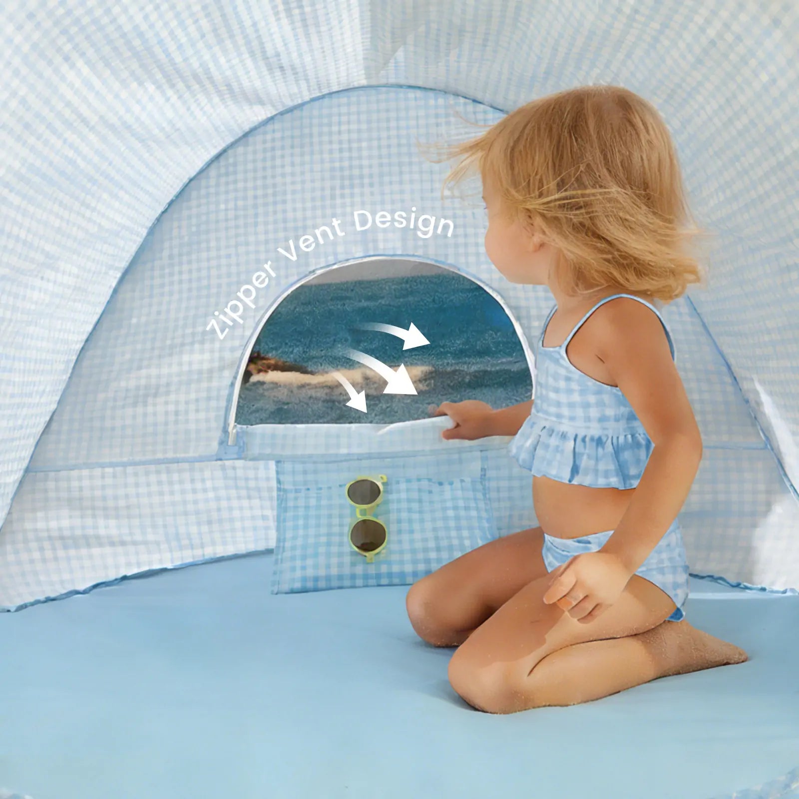 A child in a blue swimsuit kneels inside the Tiny Land® One-Stop Beach Toy & Tent Set – Light Blue Gingham, which features UV protection, a zippered mesh window, sunglasses in the inner pocket, and arrows pointing to "Zipper Vent Design.|Light Blue Gingham