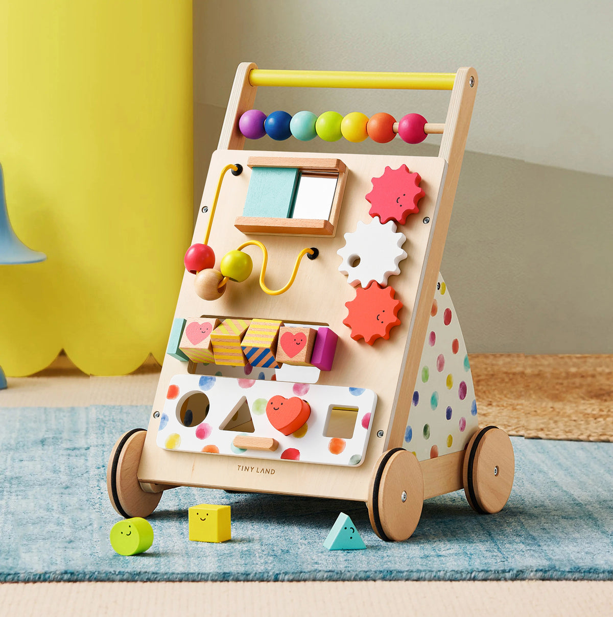 Tiny Land® Premium Natural Wooden Activity Walker featuring a rainbow design, colorful beads, spinning gears, a shape sorter, a mirror, and three small wooden shapes resting on the rug in front.