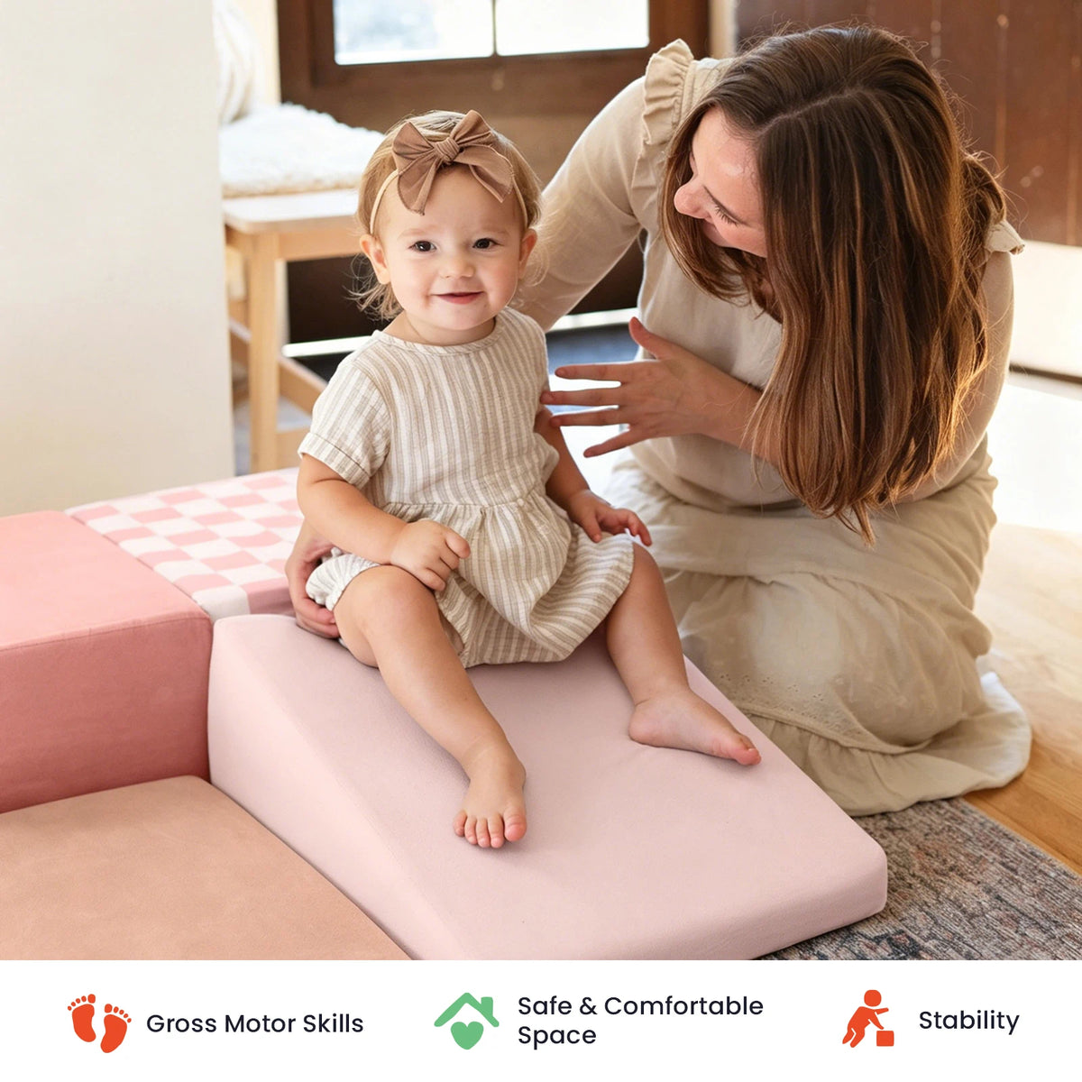 A smiling toddler sits on the Tiny Land® PlayNest Climbing Blocks - Violet, part of Tiny Land’s soft play equipment collection, while an adult woman—possibly her mother—kneels nearby. Icons below highlight benefits: gross motor skills, safe space, and stability. Sunlight streams in from a window.