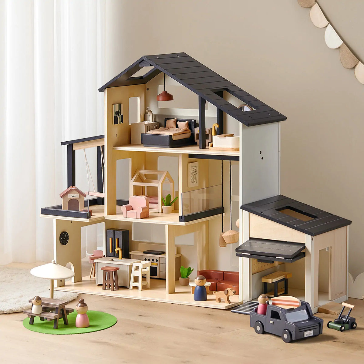 The Tiny Land Sweet Family Gift Set features a black dollhouse with a garage and extra dolls. Arranged with toy cars and accessories, it creates a playful scene that inspires imaginative play.