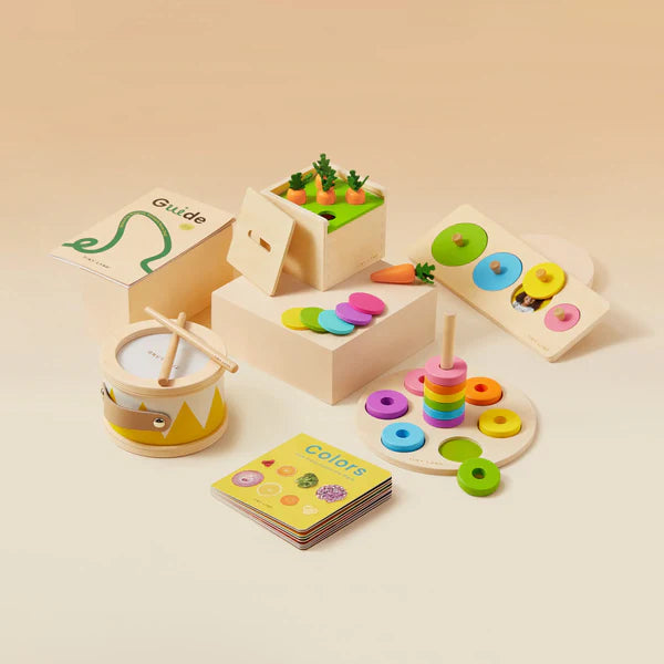The Tiny Land® Montessori Advanced Skills Baby Set (13–24 months) by Tiny Land features a drum with drumsticks, stacking ring toy, carrot harvesting game, and shape sorting boards—perfect for sensory and fine motor skill development.