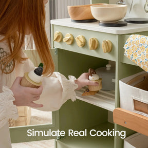 A child plays with toy cupcakes and the Tiny Land® Wooden Play Kitchen with Storage for Creative Toddlers by Tiny Land. The oven door is open, displaying the text “Simulate Real Cooking.” The scene features pretend cookware on stovetop burners, functional knobs, and a floral-patterned cloth.|sage