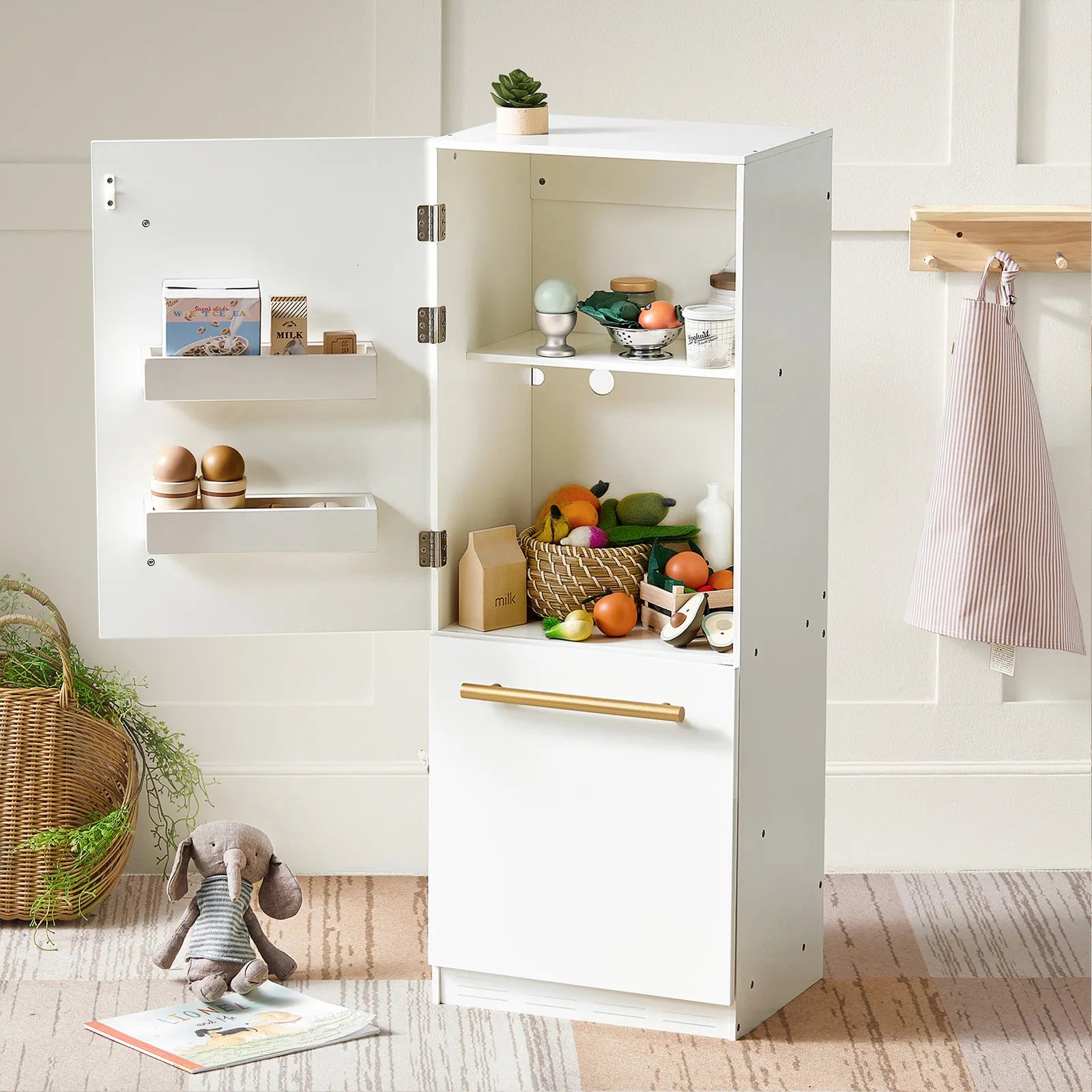 The Tiny Land® PopJoy Kitchen & Fridge Set features a white kids’ kitchen with an open fridge displaying toy eggs, milk, and veggies. A toy rabbit and wooden eggs sit nearby, with a striped apron hanging on the wall—perfect for pretend play.