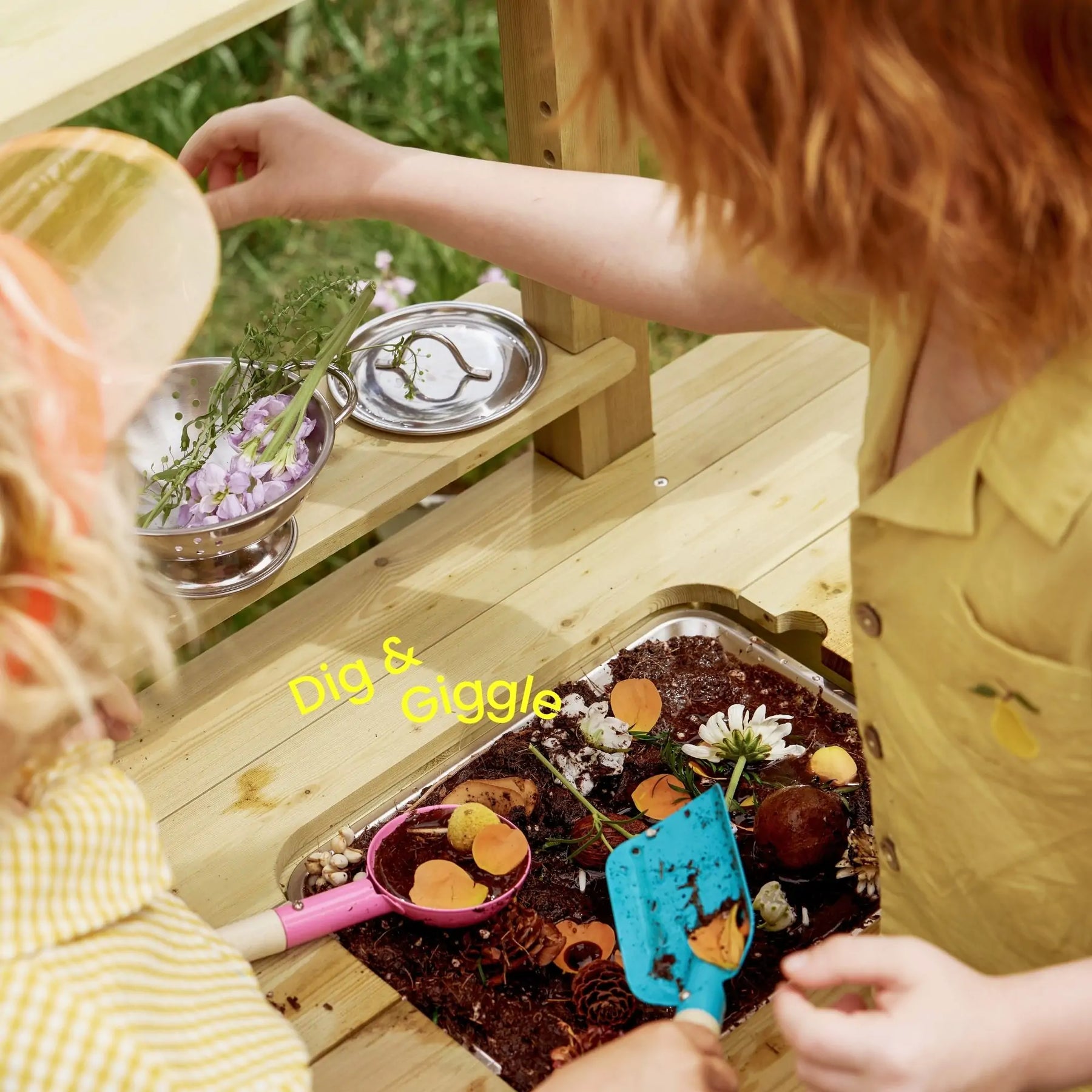 Two children using utensils and flowers on Tiny Land® DuoPlay Mud Kitchen table