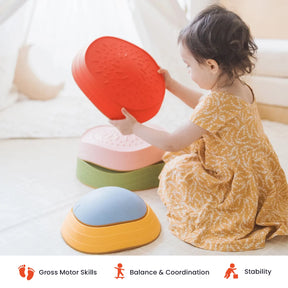 A toddler in a yellow dress plays with the Tiny Land® Stepping Stones - Vintage Color by Tiny Land indoors, transforming the room into a fun obstacle course. Icons below highlight benefits: gross motor skills, balance and coordination, and stability.