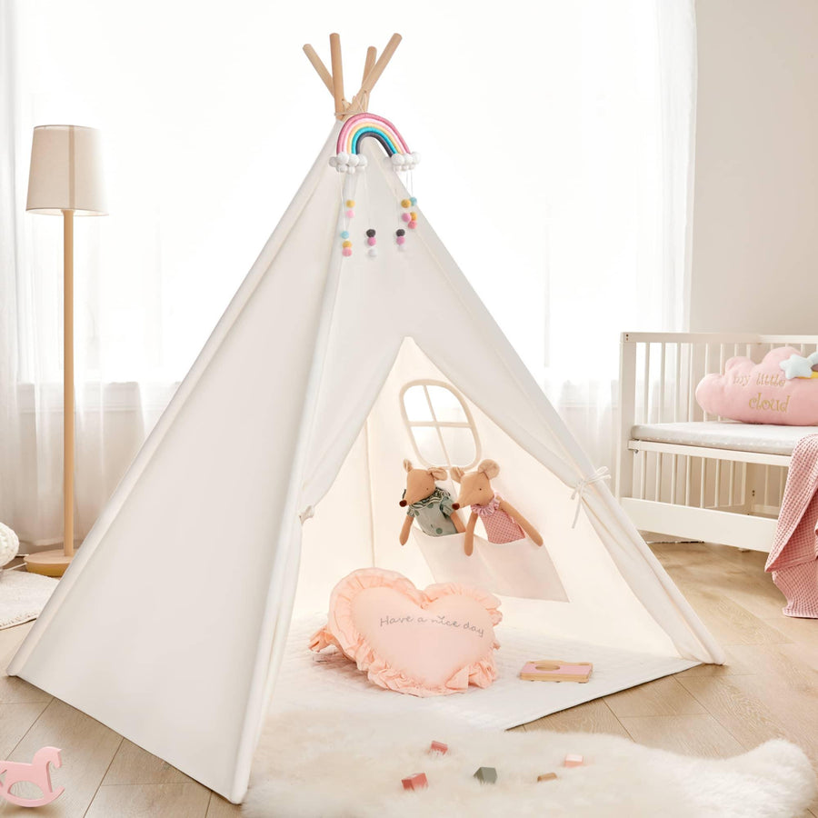 A cozy kids’ room features a white play tent with a rainbow and pom-poms, two plush animals from the Tiny Land® Mystery Surprise Box, a heart pillow, premium wooden toys on the floor, a crib, and soft natural light through curtains.
