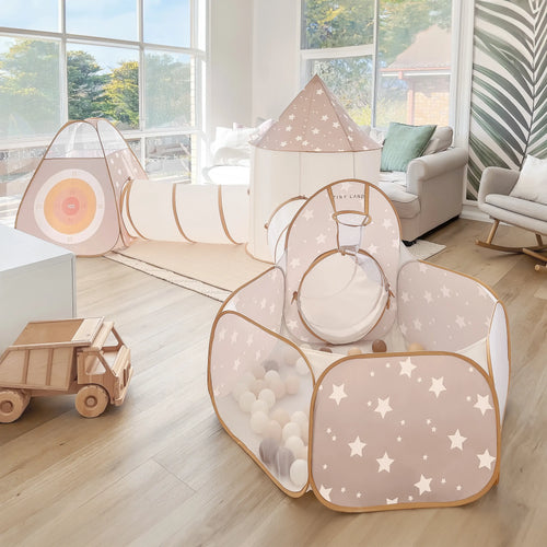 A bright playroom with a star-patterned play tent set, wooden toy truck, cozy armchair, and large windows showcases the Tiny Land® Discovery 5-in-1 Play Tunnel (no balls), target, and a pastel ball pit.