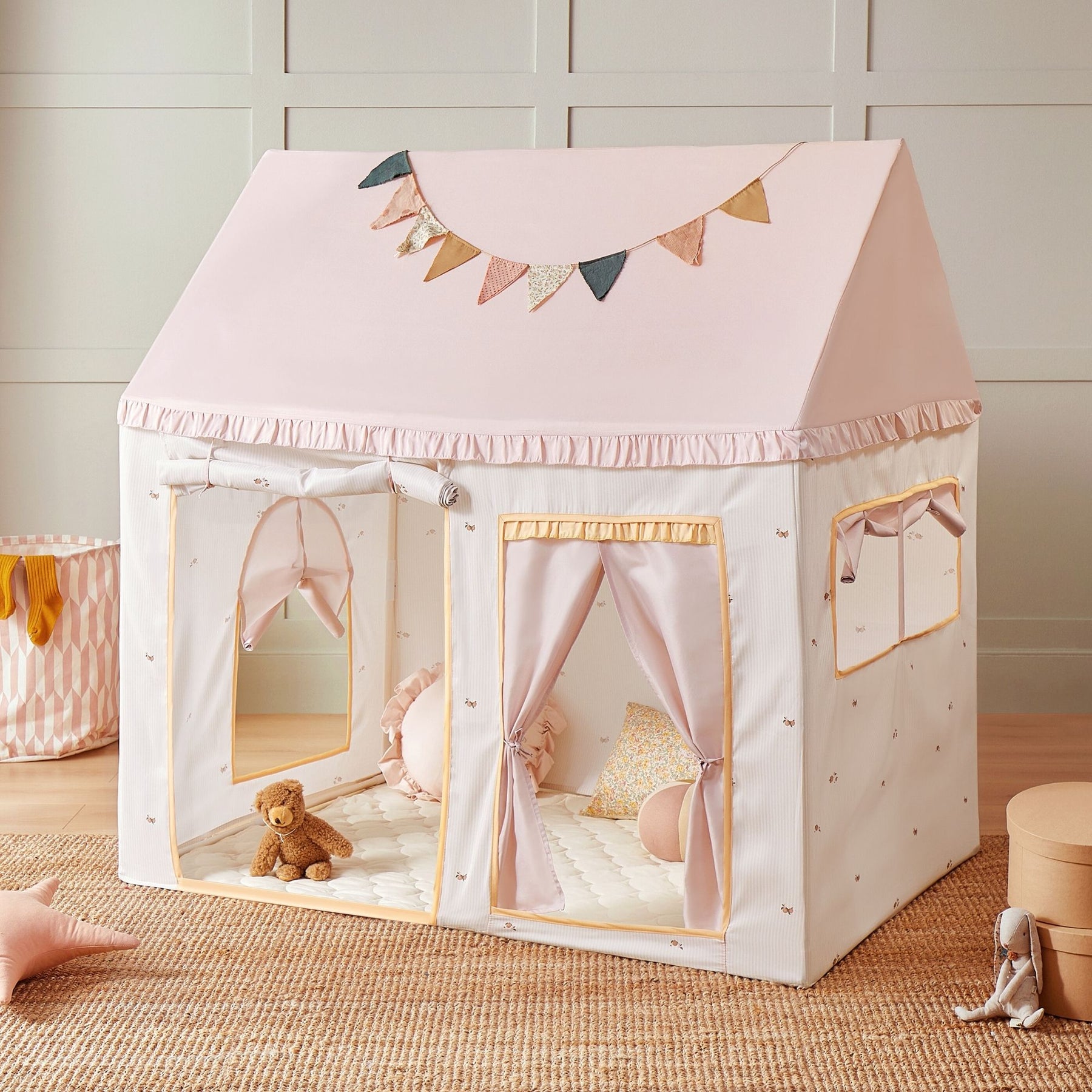 The Tiny Land Sweet Dreams Playset features a pink dollhouse and a pink-white house-shaped play tent, adorned with colorful bunting. Plush toys, pillows, and mini furniture inspire imaginative play in the softly lit room.