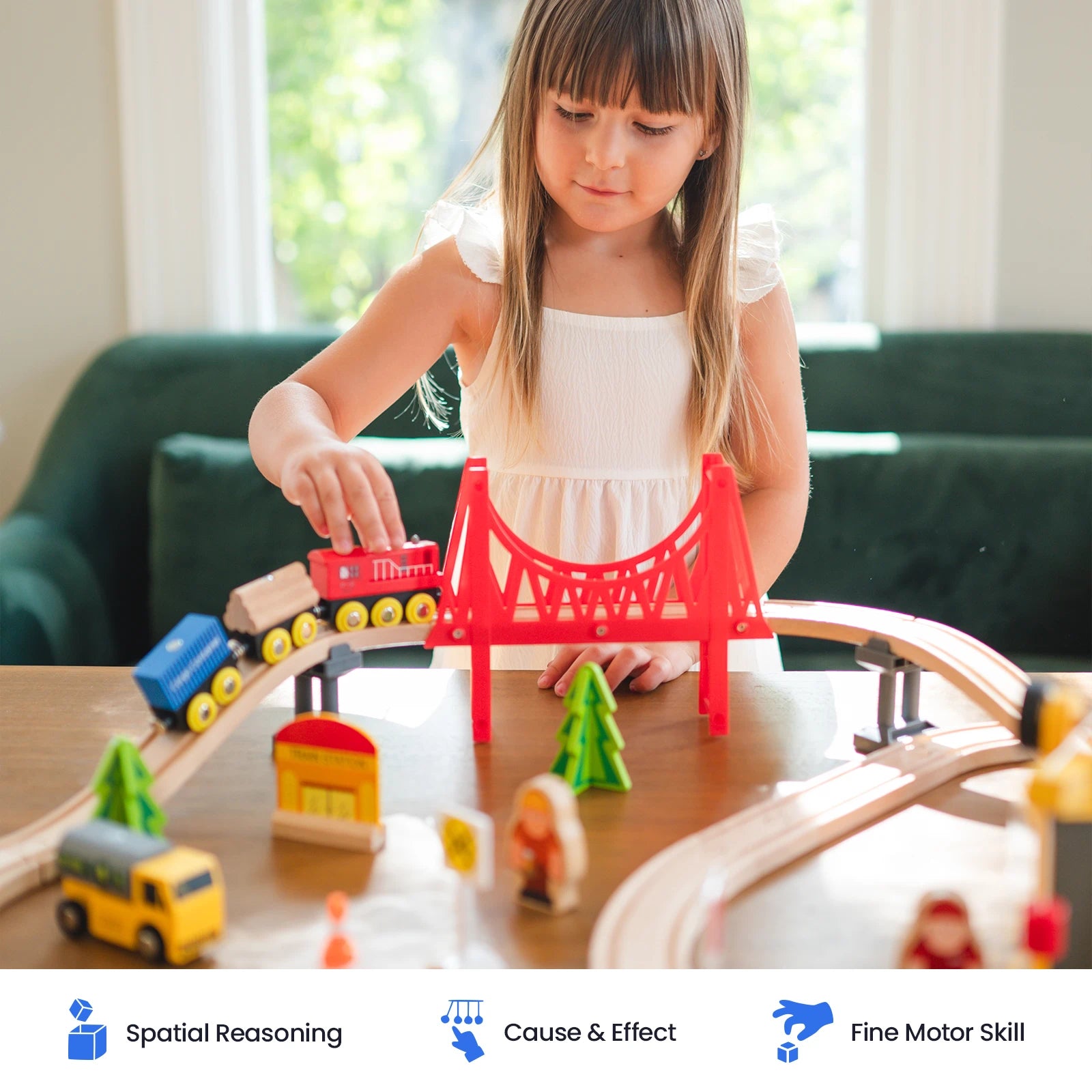 A young girl in a white dress plays with the Tiny Land® Wooden Train Set for Children on a table, guiding trains over a vibrant red bridge and along wooden tracks. Colorful toy vehicles, trees, and buildings from Tiny Land are arranged around the set. Three icons at the bottom emphasize that this Tiny Land train set is compatible with major wooden railway brands and made from sustainable wood.|39 Pcs
