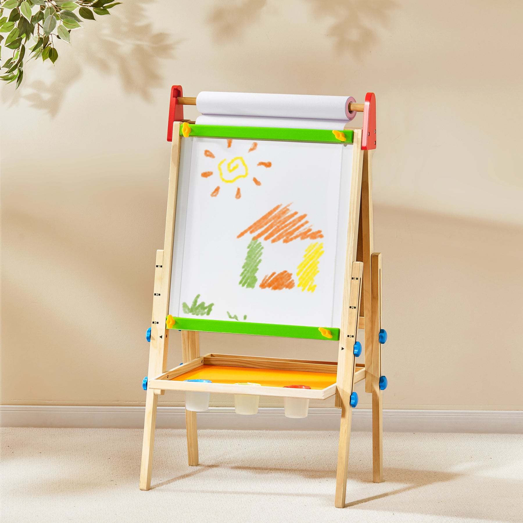 The Tiny Land Bright Play & Art Set features a height-adjustable easel with whiteboard, art paper roll, blue knobs, and a tray with three white containers. A colorful drawing decorates the easel beside the cream playhouse with lights.