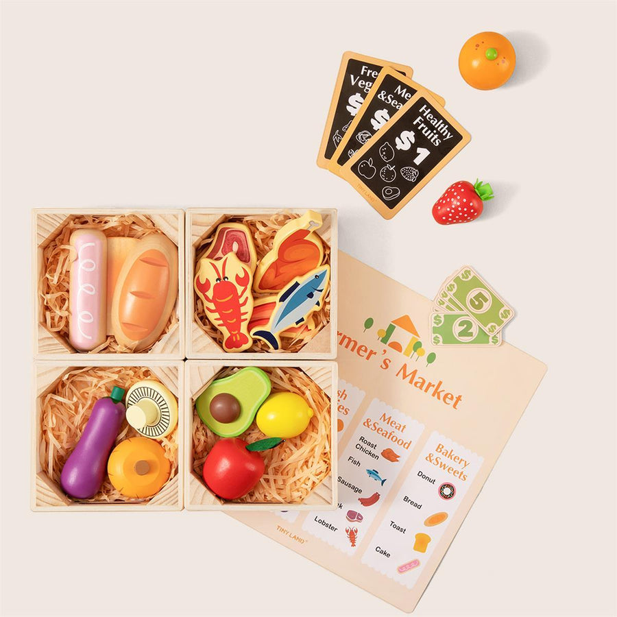 Tiny Land Play Food’s Wooden Food for Play Kitchen & Wooden Rack includes bread, seafood, vegetables, and fruit in four crates with play money, cards, a die, and a Farmer’s Market shopping list arranged on a light background.
