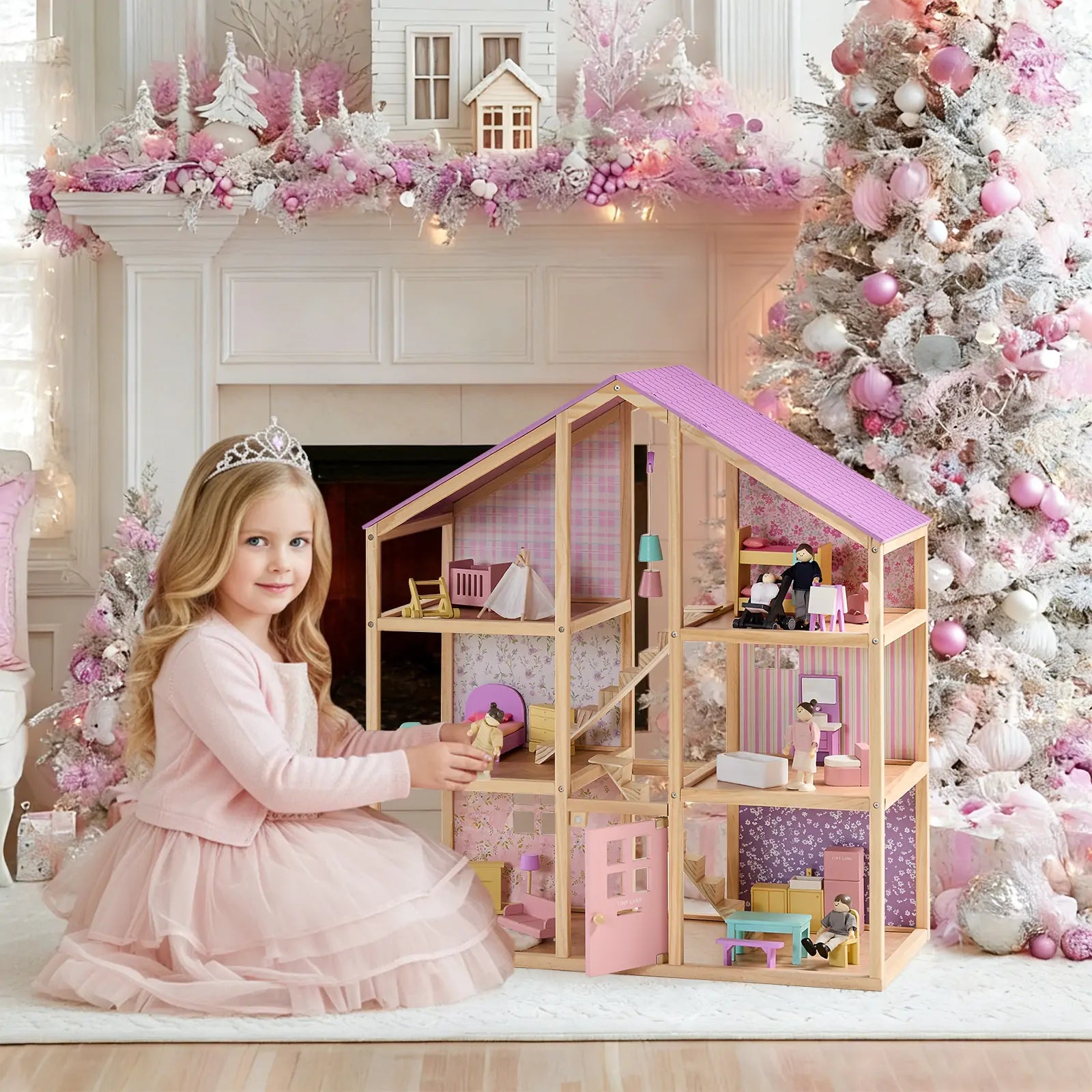 A young girl in a pink dress and tiara plays with the Tiny Land® Sweetwood Unicorn Dollhouse & Wooden Dollhouse Dolls by Tiny Land, surrounded by festive décor, a Christmas tree, and pink ornaments in a beautifully decorated room.