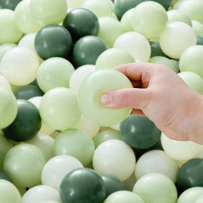 A hand holds a Tiny Land® Green Ocean Ball over a pile of safe, non-toxic play balls in light green, dark green, and off-white from the 200-piece Tiny Land® Green Ocean Ball set.