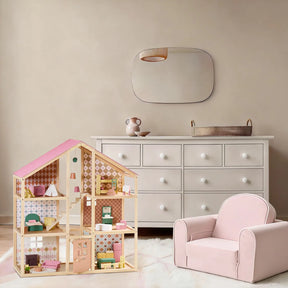 A pastel children’s room featuring the Tiny Land® Sweetwood Pegasus Dollhouse with Wooden Dollhouse Dolls, a pink chair, white dresser with decor, and a modern mirror on a beige wall.