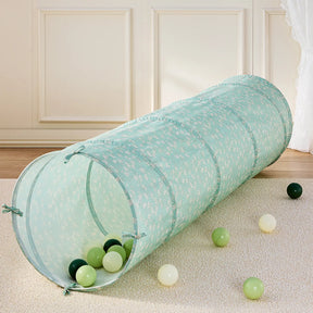 The Tiny Land® PlayNest Climbing Ball Pit Set with Tunnel features a light blue tunnel with a floral pattern, resting on a beige carpet and surrounded by green, white, and yellow balls—perfect for an inviting indoor playground.