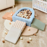 The Tiny Land® PlayNest Climbing & Ball Pit Set features climbing blocks, foam ramps, a checkered block, and a blue ball pit with pastel balls—perfect for toddlers' indoor play. A white crib and beige furniture sit on a tan carpeted floor in the background.|Blue