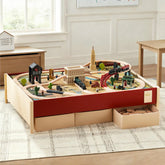 The Tiny Land® 1920 Railway Adventure Train Table by Tiny Land INC features an interactive city playset with tracks, bridges, and buildings. Two drawers store extra pieces, while the table sits on a patterned rug in a bright, tidy room.